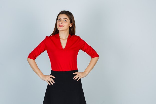 Young woman holding hands on hips in red blouse, black skirt and looking cheery