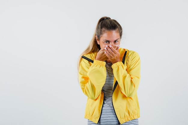 Free photo young woman holding hands on mouth in t-shirt, jacket and looking happy. front view.