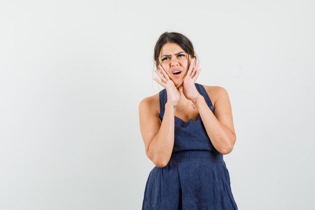 Young woman holding hands near mouth in dress and looking displeased