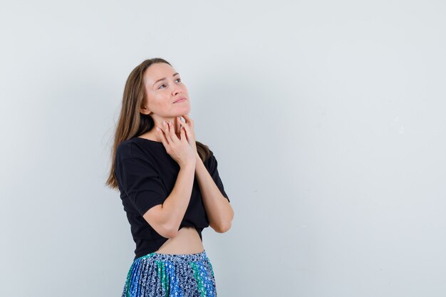 Young woman holding hands on neck in black t-shirt and blue skirt and looking happy