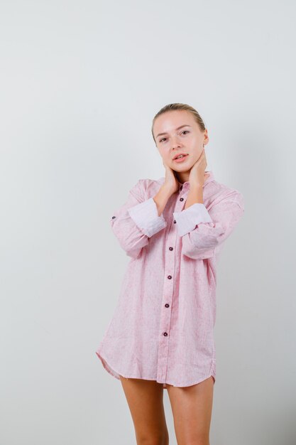 Young woman holding hands on neck in pink shirt and looking alluring
