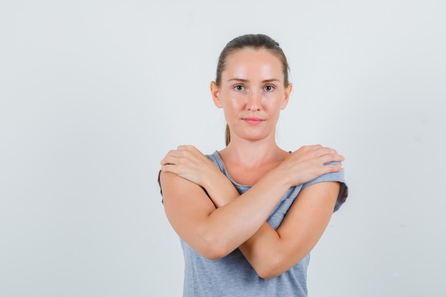 Giovane donna che tiene le mani sulle spalle in maglietta grigia e che sembra sicura. vista frontale.