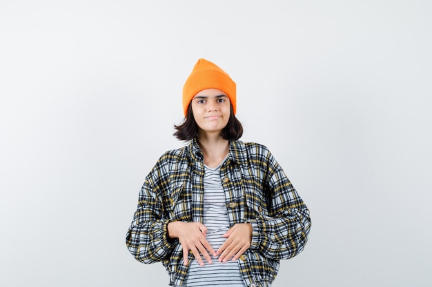 Young woman holding hands on stomach in orange hat looking pleased