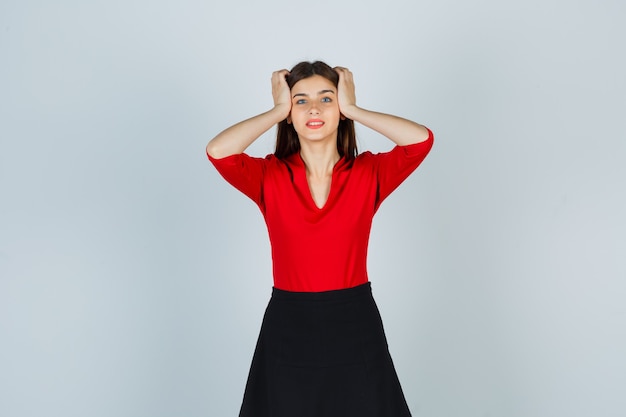 Молодая женщина, держащая руки на висках в красной блузке