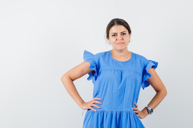 Free photo young woman holding hands on waist in blue dress and looking confident