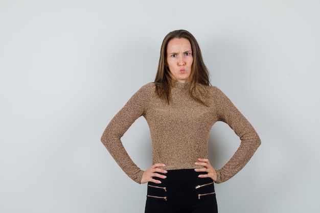 Foto gratuita giovane donna che tiene le mani sulla vita in maglione dorato e pantaloni neri e sembra sorpresa