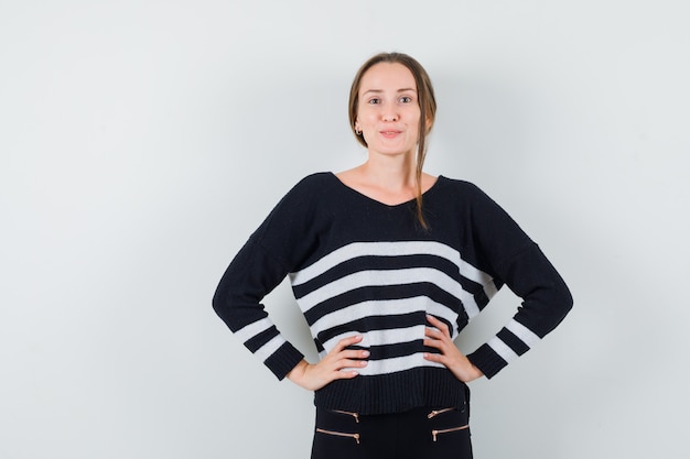 Free photo young woman holding hands on waist in striped knitwear and black pants and looking confident