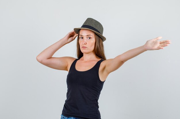 일 중항, 반바지 전면보기에서 팔을 스트레칭하는 동안 모자를 들고 젊은 여자.