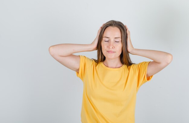 黄色のTシャツに手で頭を抱えて疲れている若い女性