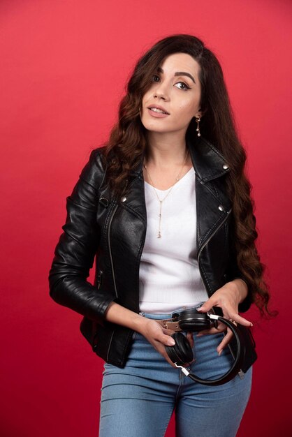 Young woman holding headphones and posing on a red background. High quality photo
