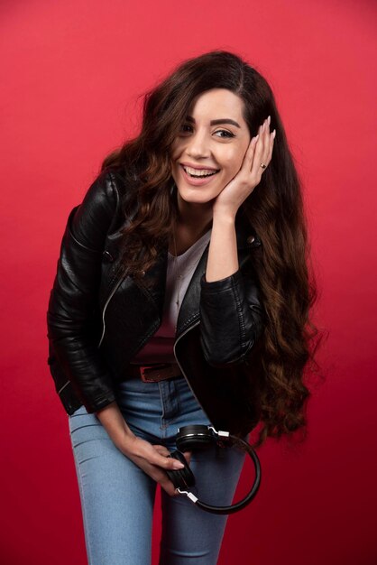 Young woman holding headphones and posing on a red background. High quality photo