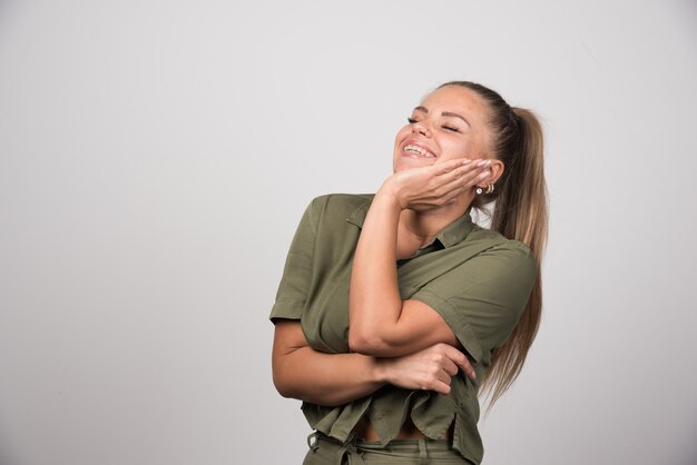 Young woman holding her cheek on gray wall.