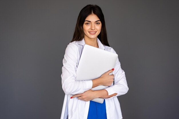 Young woman holding laptop and looking at camera over gray background