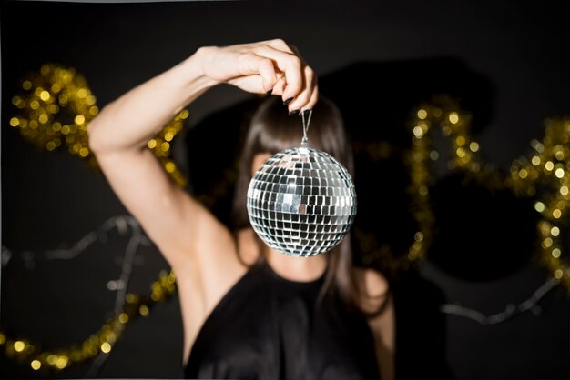 Young woman holding little disco ball near tinsel