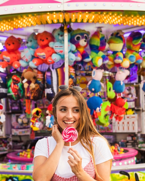 Young woman holding lollipop in her hand standing in front of toy shop