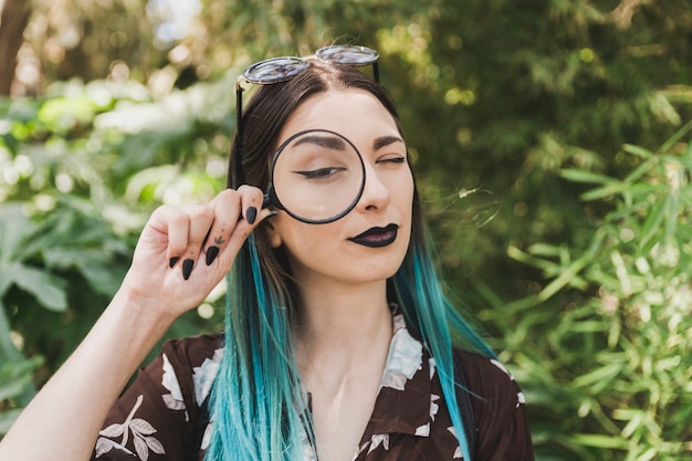 Free photo young woman holding magnifying glass over the one eye