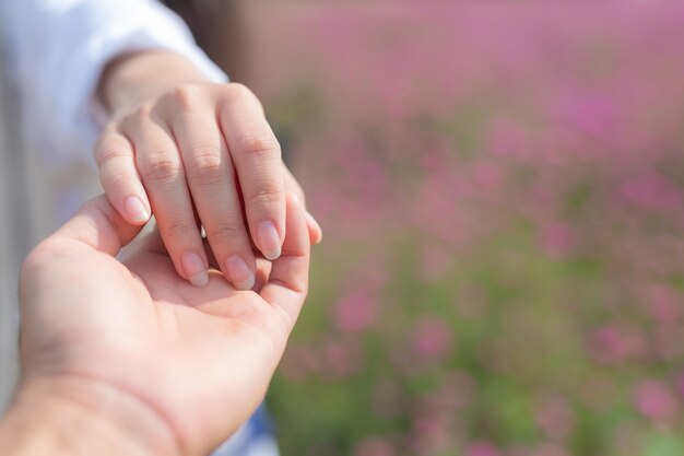 花の庭で彼を導きながら男の手を握る若い女性