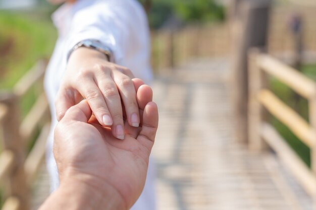 Young woman holding man hand while leading him on flower garden