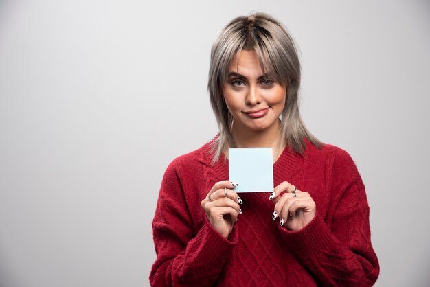 Young woman holding memo pad on gray background.