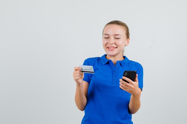 青いTシャツと幸せそうに見える携帯電話とプラスチックカードを保持している若い女性