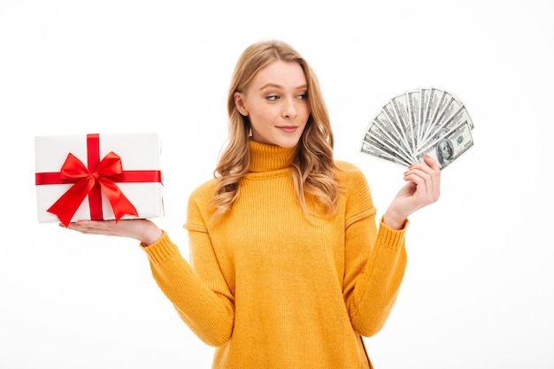 Free photo young woman holding money and surprise gift box.