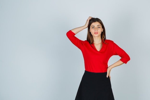 Young woman holding one hand on head, another hand on hip in red blouse