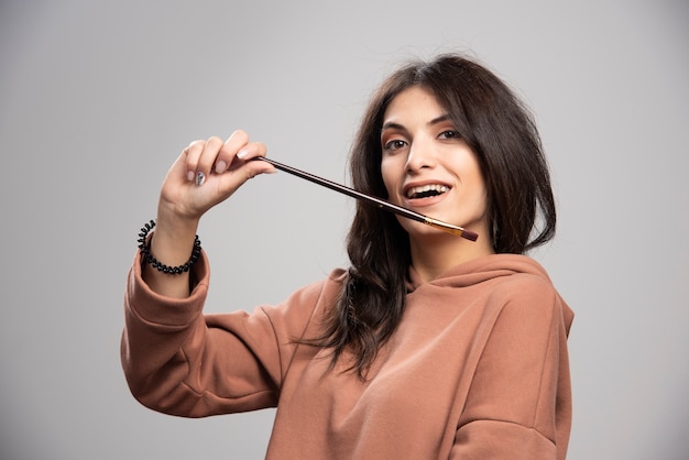 Young woman holding paint brush on gray