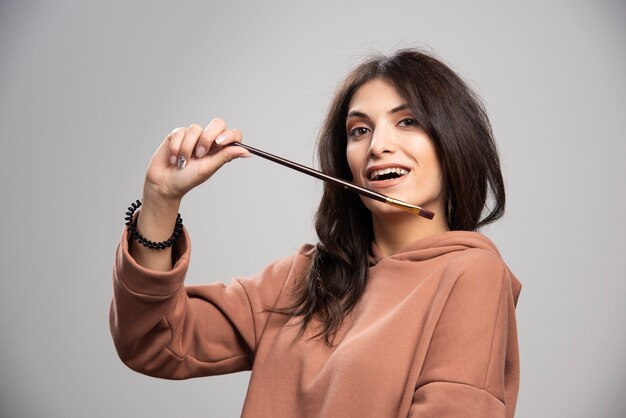 Young woman holding paint brush on gray