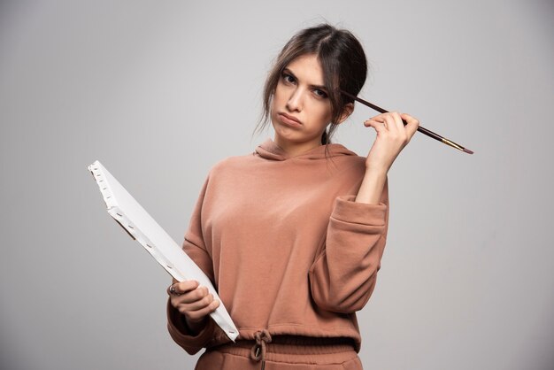 Young woman holding paint brushes and canvas