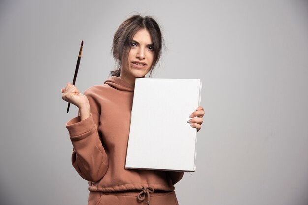 Young woman holding paint brushes and canvas