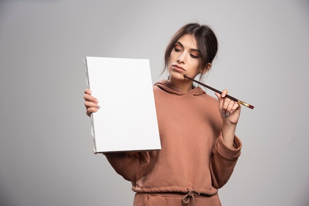 Young woman holding paint brushes and canvas