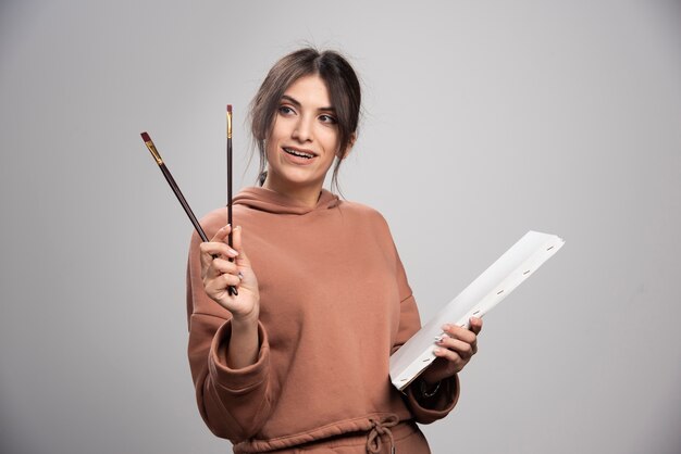 Young woman holding paint brushes and canvas