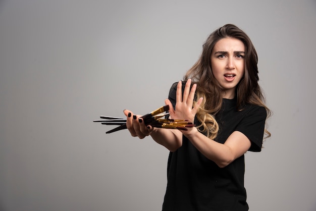 Young woman holding paint brushes on gray wall. 