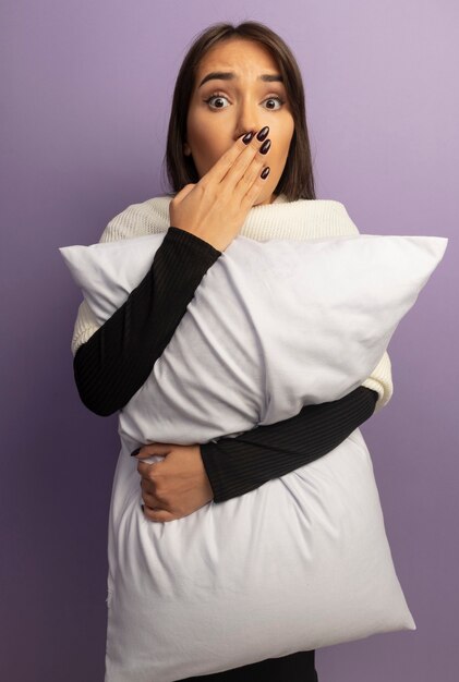 Молодая женщина, держащая подушку в шоке, прикрывает рот рукой