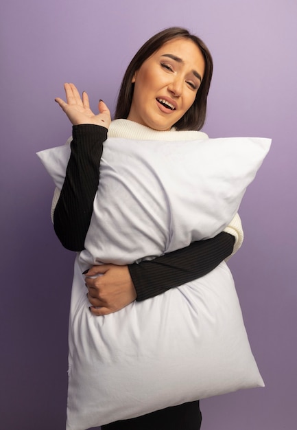 Молодая женщина, держащая подушку, улыбаясь со счастливым лицом, машет рукой