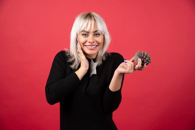 Young woman holding a pinecone on a red wall. 