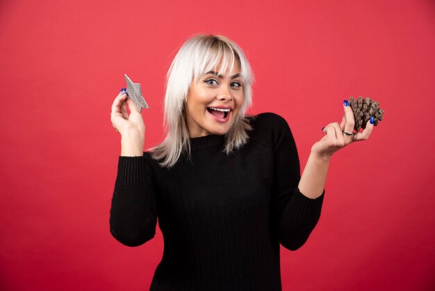 Young woman holding a pinecone with a star on a red wall. 