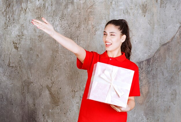 핑크 선물 상자를 들고 젊은 여자는 흰색 리본으로 포장 하 고 누군가를 가리키는.