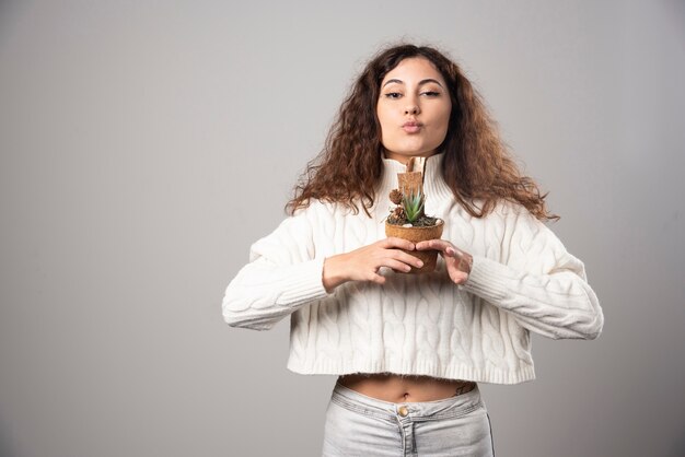 灰色の壁に植物を保持している若い女性。高品質の写真