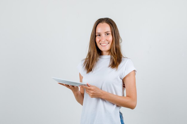 Young woman holding plate in white t-shirt, shorts and looking merry