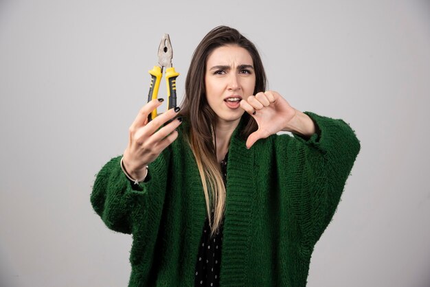 Young woman holding pliers and showing a thumb down.