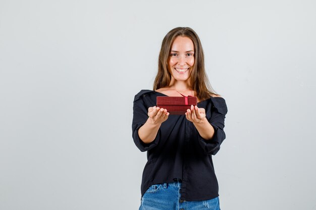 Young woman holding present box in shirt, shorts and looking happy