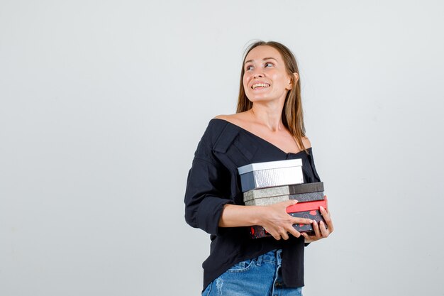 Young woman holding present boxes while looking back in shirt, shorts front view.