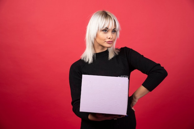 Young woman holding a present on a red wall. 