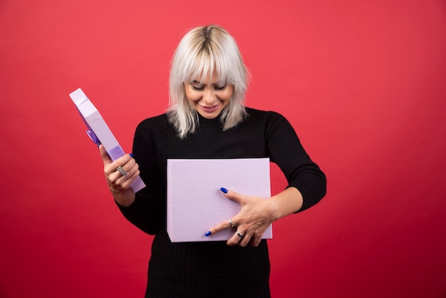 Free photo young woman holding a present on a red wall.