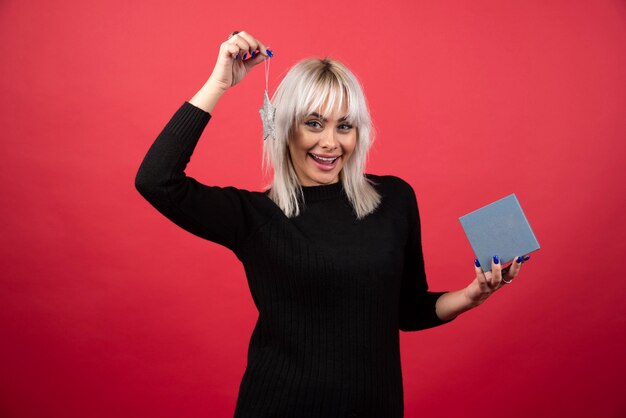 Young woman holding a present with a star on a red wall. 