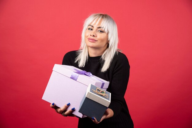 Young woman holding presents on a red wall. 