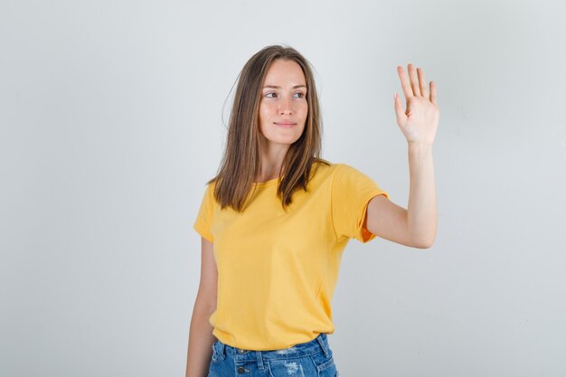 Young woman holding raised hand open and smiling in t-shirt