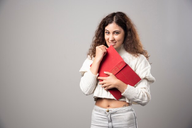 Young woman holding red book on a gray wall. High quality photo