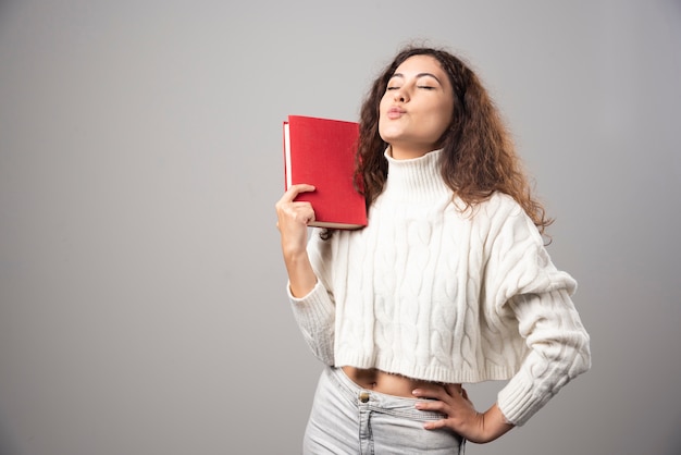 Giovane donna che tiene il libro rosso su un muro grigio. foto di alta qualità